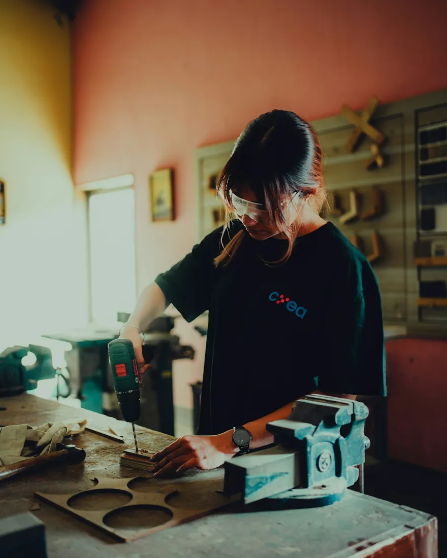 Manos lijando una pieza de madera clara sobre un banco de taller